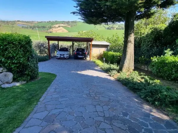 La strada pavimentata nel giardino, che porta al portico con due posti auto coperti.